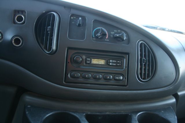 Dashboard of Ford E-Series van showing radio and climate controls. Knobs labeled for AC, fan, and temperature with vents on either side.