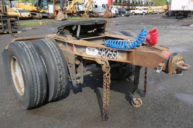 Trailer dolly chassis with dual rear tires, identification plate reading 58255, chains hanging, blue coiled air hose, red hose, weathered brown frame.
