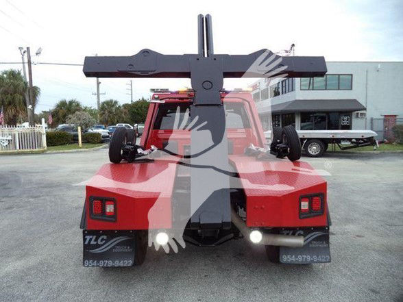 Back of a red tow truck with a heavy-duty hitch arm and rear lights. License-like stickers and numbers visible on mudflaps: 954-979-842? (blurred).