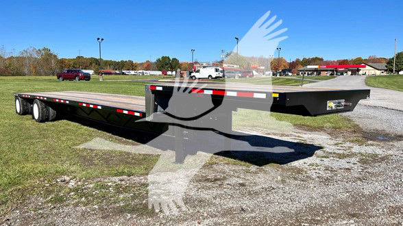 Manac steel drop deck trailer in a parking lot, side view showing dual rear axles and lower deck, stock number placard visible.