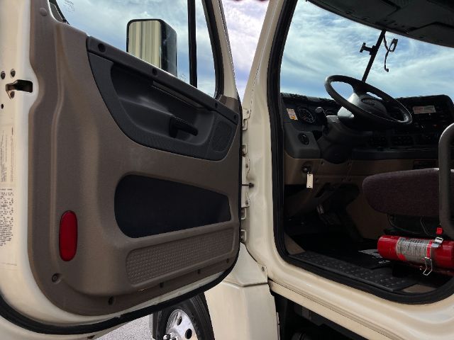 Truck cab interior with open door showing steering wheel, dashboard, and seat. Visible text includes no legible labels on the door panel or dashboard.