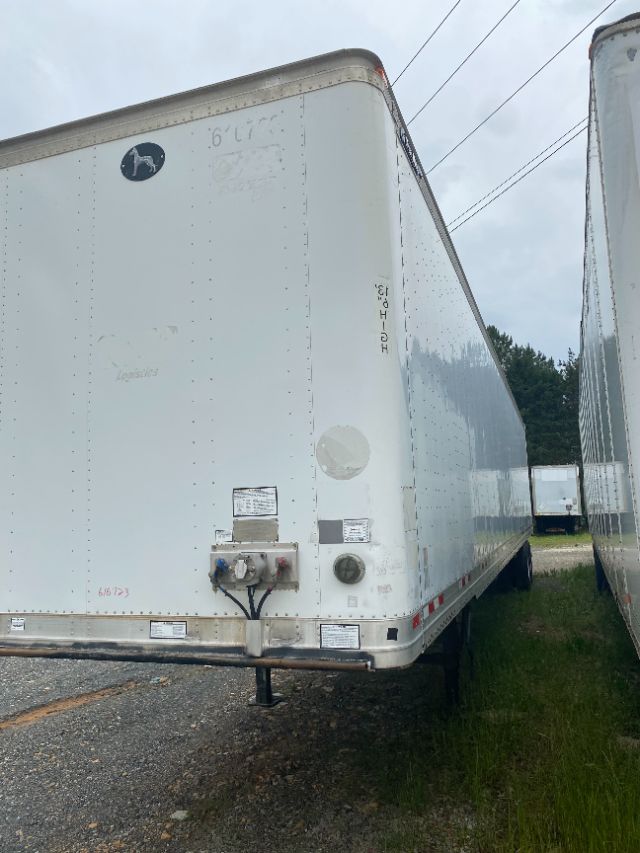 Trailer side with John Deere logo and multiple labels, rear corner of a white Wabash Duraplate trailer showing electrical box, hoses, and bumper.