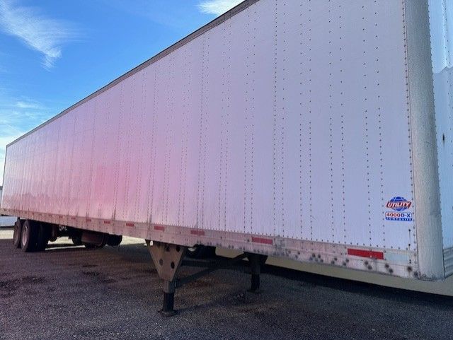 Utility 4000DX trailer side view showing top rail and undercarriage with landing gear and front wheel, white aluminum skin with small badge near rear.