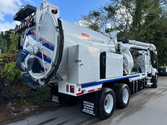 Vacuum truck with large cylindrical tank and rear-mounted chute, Freightliner/ Hagcon branding on side, multiple axles and hoses visible.