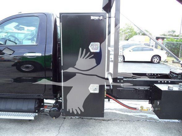Truck cab with a black storage box mounted behind the cab showing hydraulic lines and chassis details.