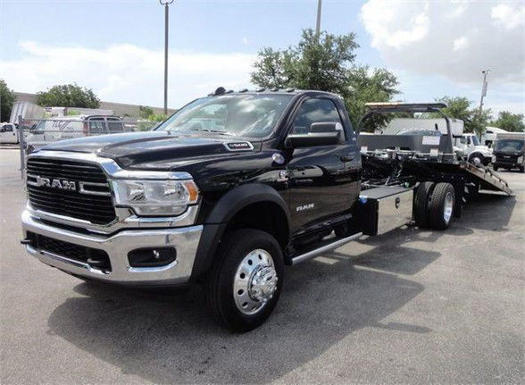 RAM tow truck with a flatbed on a black 2024 Ram 5500 SLT front view showing chrome grille, dual side mirrors, and wheel set.