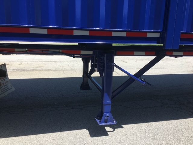 Trailer landing gear and support frame of a blue utility dump trailer, showing crowned support legs and cross braces.