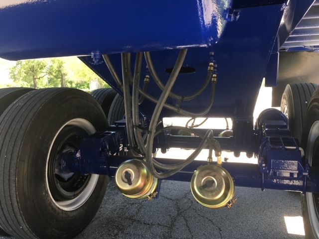 Underbelly of a blue utility trailer showing hydraulic lines, hoses, and two circular air tanks near the axle. Large tires on both sides.