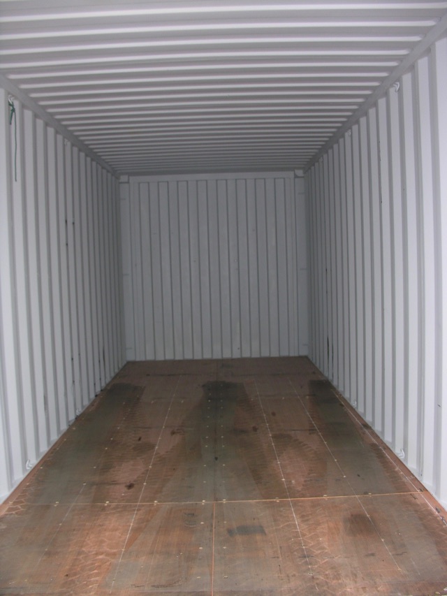 Interior of an empty enclosed shipping container trailer showing wooden floor and corrugated metal walls and ceiling.
