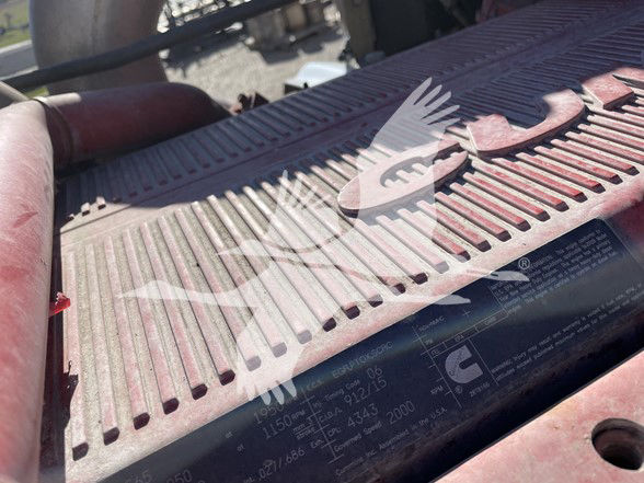 Tractor-trailer engine bay cover with embossed and printed labels, showing a Kenworth component with serial/part information obscured by glare.