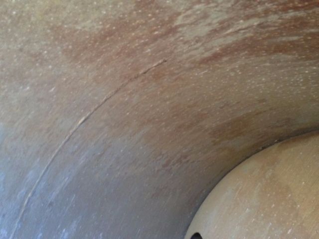 Image shows a close-up view of a rounded metallic surface with a curved seam or crack and a beige circular component protruding.