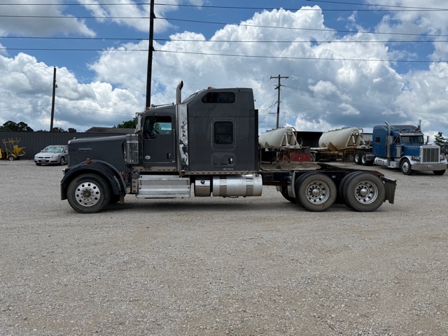 Kenworth W900 tractor in a gravel lot, side profile view, with a sleeper cab and dual rear axles.