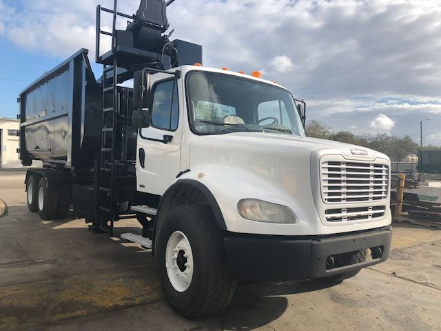 2007 Freightliner M2-112 grapple truck in a light color with a large hydraulic grapple on the rear chassis; side view shows front bumper, grille, and cab.