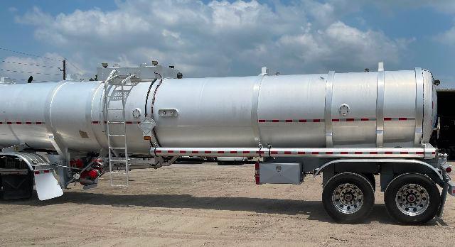 Crude oil tanker trailer with aluminum DOT-407 designation, cylindrical tank, dual rear axles, ladder and access hatch visible.