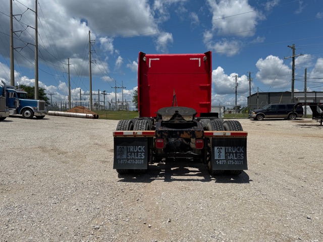 Rear view of a red Peterbilt truck chassis on a gravel lot, with mudflaps showing 'Truck Sales' and phone number.