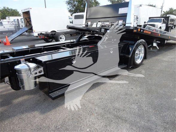 Peterbilt 337 tow truck chassis showing flatbed with black paint and chrome wheels, side view of frame and wheel, stock number J03058.