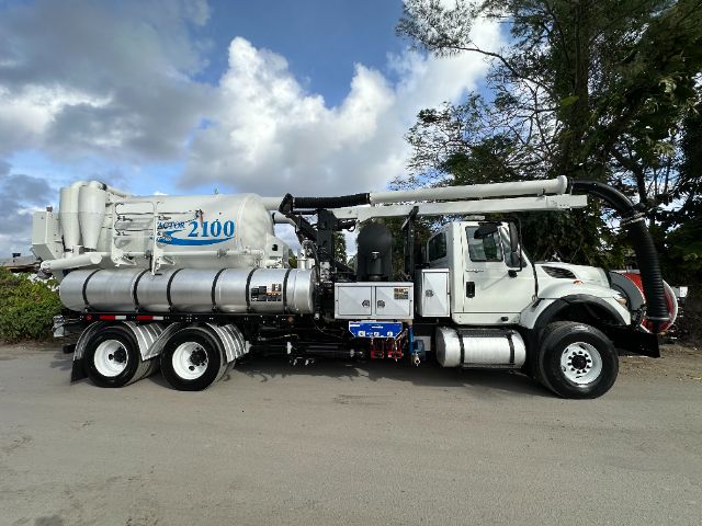 Vehicle side view of a white 2014 International 7500 vacuum truck with a large blue and white vacuum unit labeled AVERA 2100 on the side, fed by hoses and storage tanks.