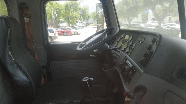Peterbilt truck cab interior with dashboard gauges, steering wheel, gear selector on floor, gray seats. Driver area visible.