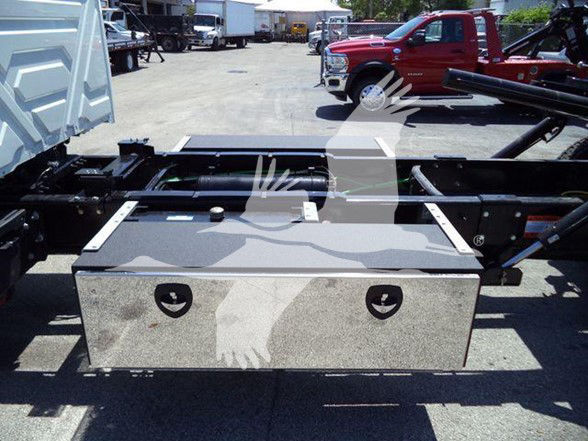 Truck chassis with a rectangular metal toolbox mounted behind the cab area, showing two circular cutouts and a flat, polished surface. Tow configuration with frame rails and hitch area visible in background.