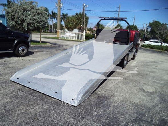 Isuzu NPR XD flatbed tow truck with a long metal ramp and open cab.
