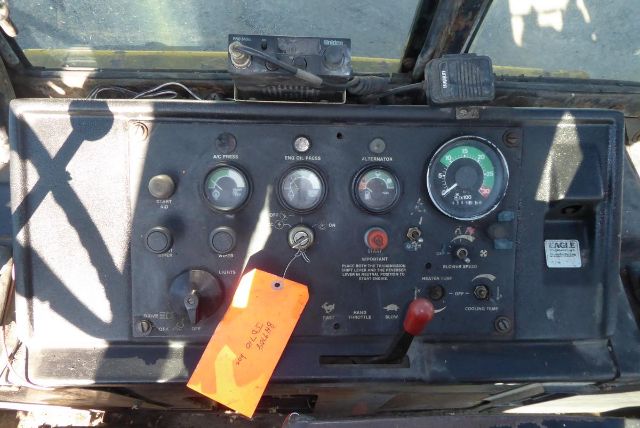 John Deere backhoe operator panel with multiple gauges, switches, and an orange tag hanging from the lever.