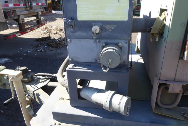 Truck equipment with a gray control panel showing a circular handwheel and a cylindrical chute; power plug and warning label visible; hydraulic lines and metal frame around.