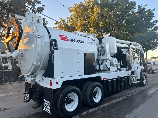 Vacuum truck labeled Vaccon with large cylindrical rear chamber and hoses, white with black undercarriage, side paneling, and multiple axles.