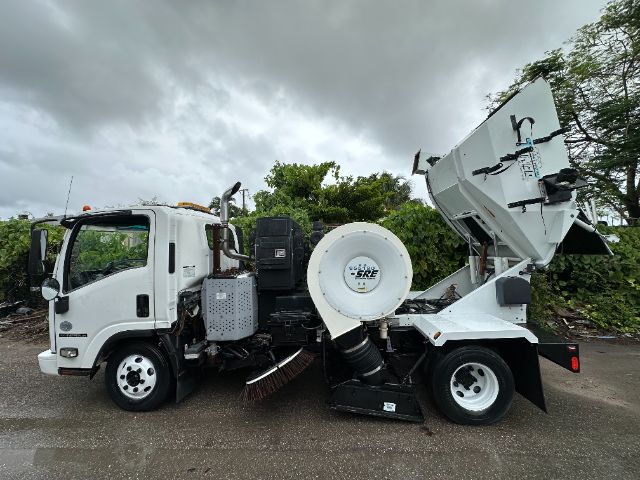 Isuzu NPR-HD street sweeper truck side view with hopper raised and rotating brush components visible.