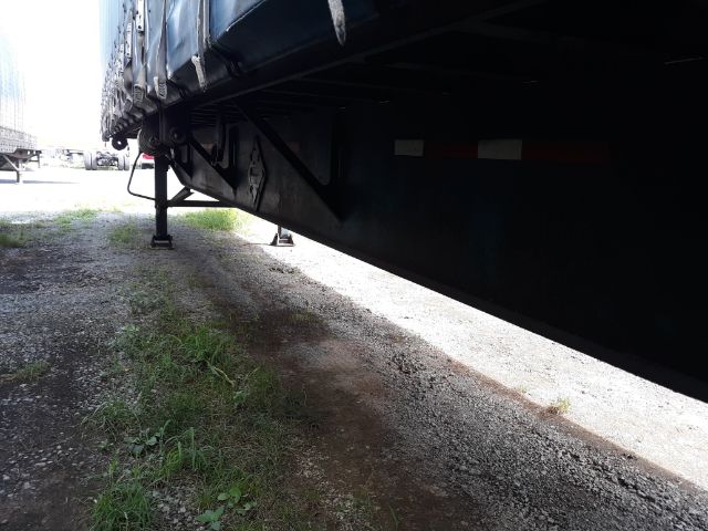 Underneath view of a black trailer with support legs visible, parked on a gravel lot.