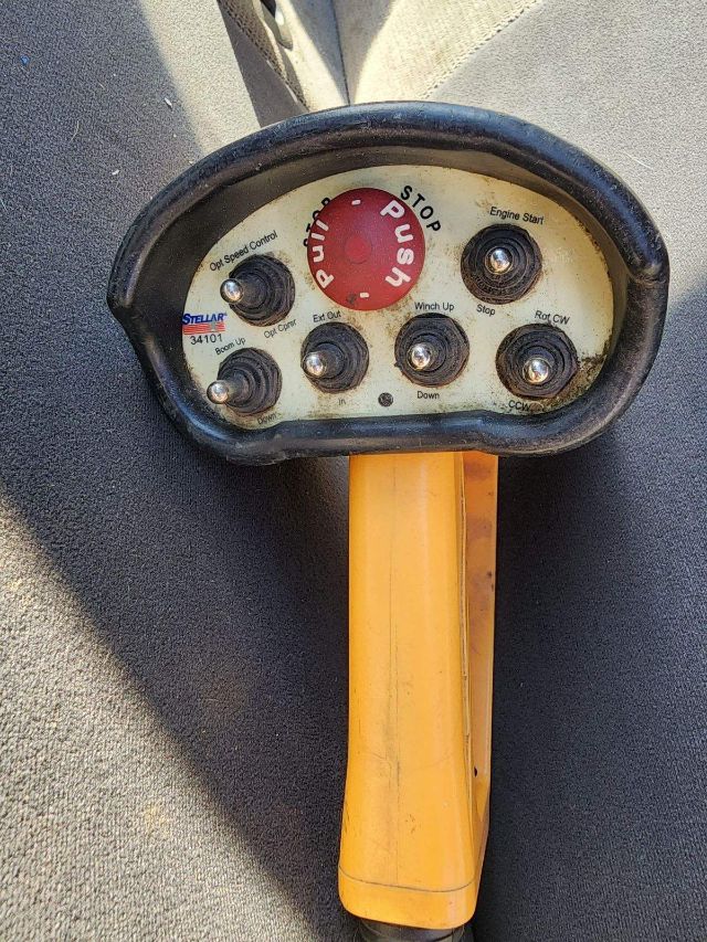 Aerial control panel of a lift with red STOP/EMERGENCY push button and multiple small black control switches labeled Up, Down, Left, Right, cw/ccw, engine start. Orange control stalk.