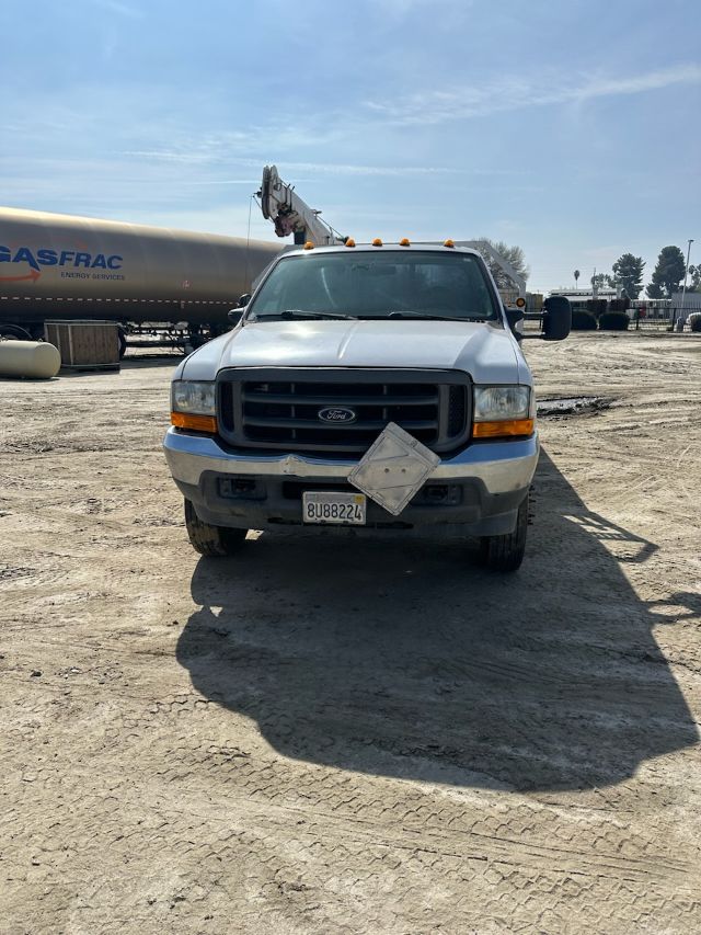 Front view of a white 2004 Ford F-550 truck with a raised boom crane in a yard, front license plate visible, diamond plate on bumper.