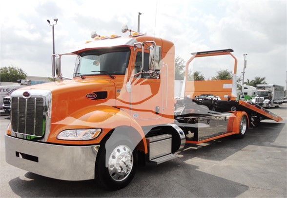 Peterbilt 337 tow truck in orange with a long wheelbase and flatbed, chrome bumper, and side mirrors.