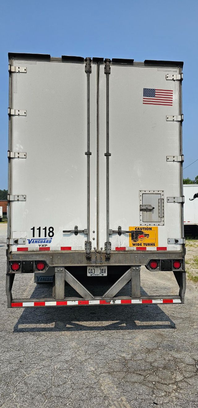 Rear view of a white Vanguard VXP trailer with dual vertical doors, American flag decal, stock number 1118, and caution sticker on right door.