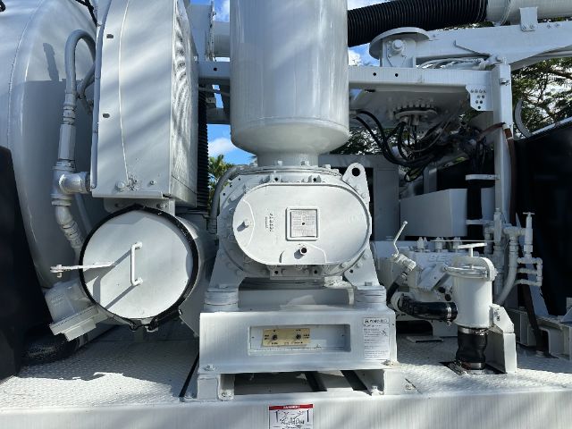 Industrial vacuum truck with large central pump, white/gray components, cylindrical hopper and control panel; visible labels and gauges on equipment.