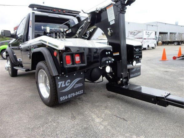 Tow truck rear with vertical lift and hitch equipment; TLC logo on mud flap and contact number 954-979-9422 visible.