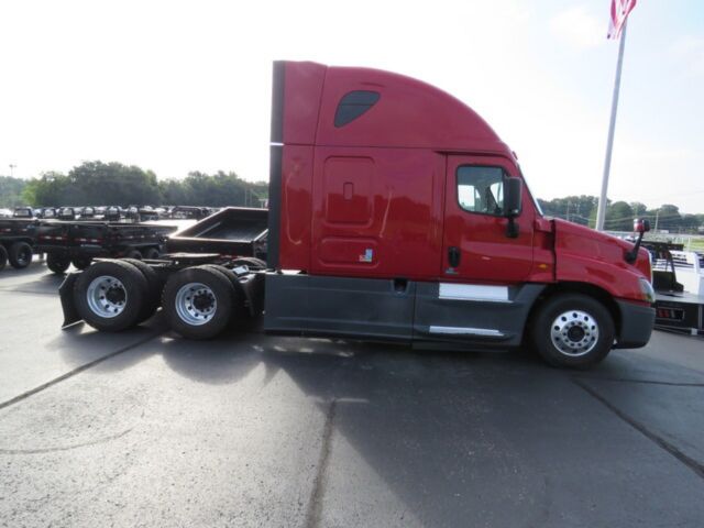Red Freightliner Cascadia Evolution semi-truck tractor in a lot, side view showing sleeper cab and dual rear axles.