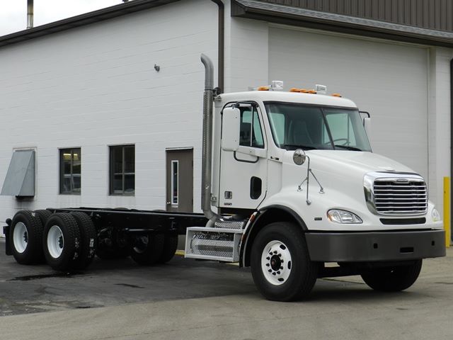 Freightliner cab and chassis truck with white cab, dual rear axles, and chrome grille showing on a paved lot.