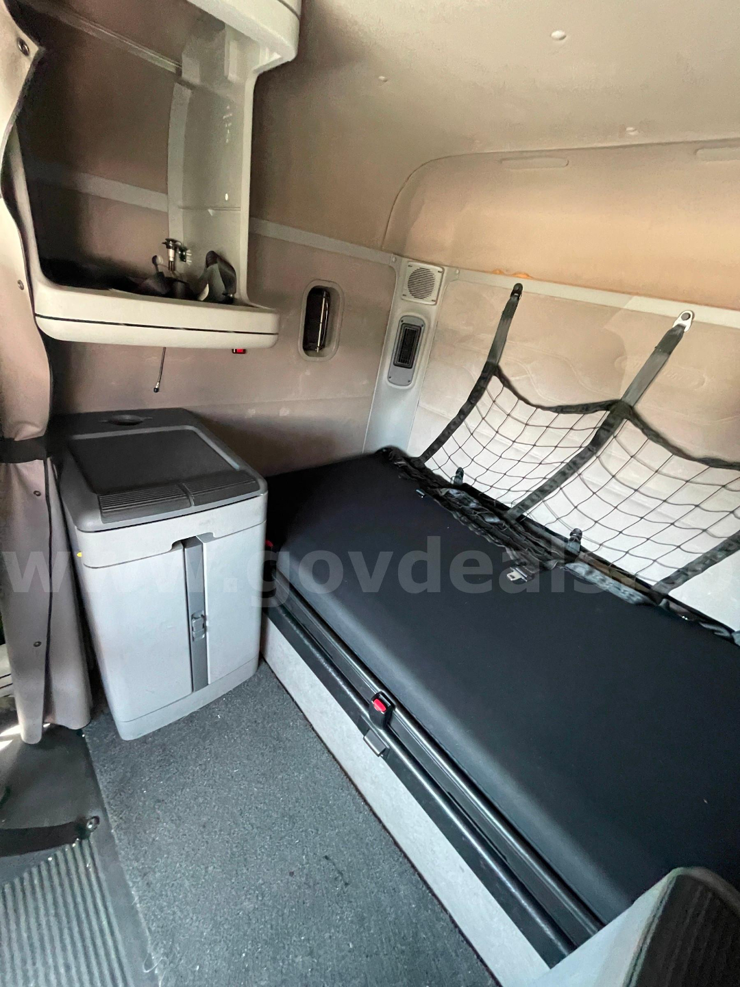 Freightliner Columbia 120 cab interior showing sleeper bunk area with black mattress, net barrier, small fridge, overhead storage, and side panel vents.