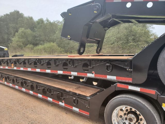 Lowboy trailer side with stacked steps and storage compartments, black metal frame, red/white reflective tape, large wheel, and hitch mechanism visible.