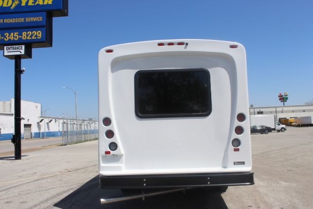 Rear view of a white 2025 Ford E450 shuttle bus with a dark window and taillights, parked in a lot.