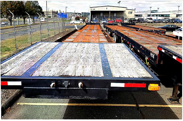 Rolloff trailer bed showing weathered wooden planks on the deck with steel frame and reflective tape; rear view including bumper, lights, and hitch area.
