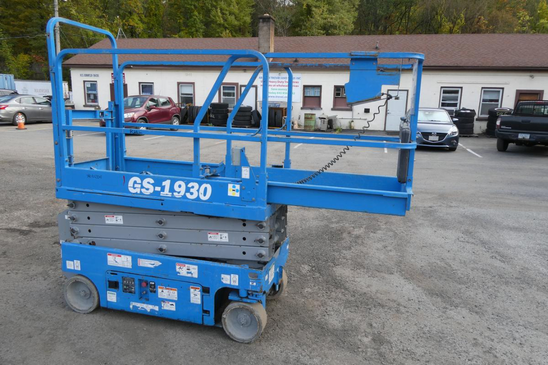 GS-1930 scissor lift in blue with label GS-1930 on side, compact base with wheels, safety rails, and control panel area visible.