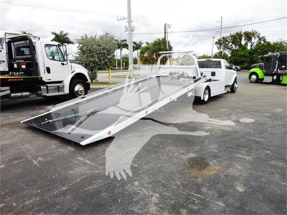 Ram 5500HD tow truck with a long white rollback bed in a parking lot.