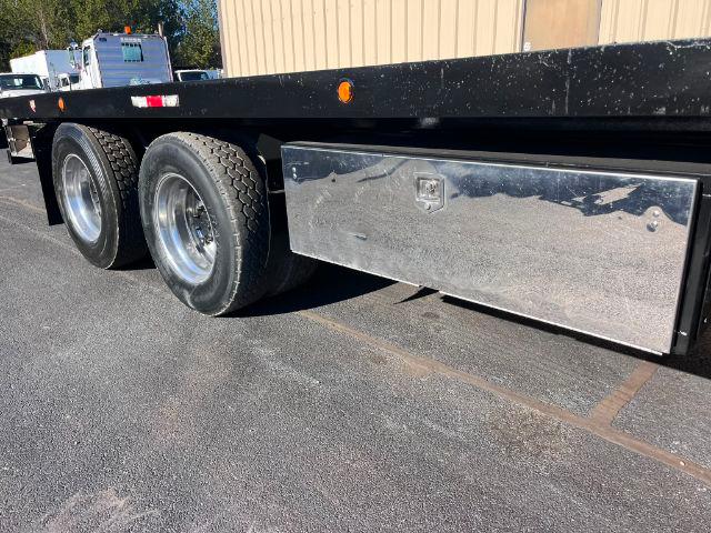 Flatbed trailer with dual rear tires and a long chrome side tool/storage box under the frame.