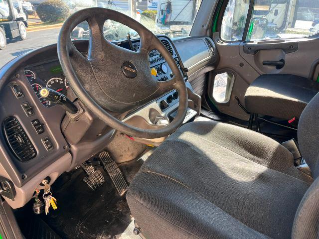 Freightliner M2 106 cab interior showing steering wheel, dashboard, and driver seat from the left side.