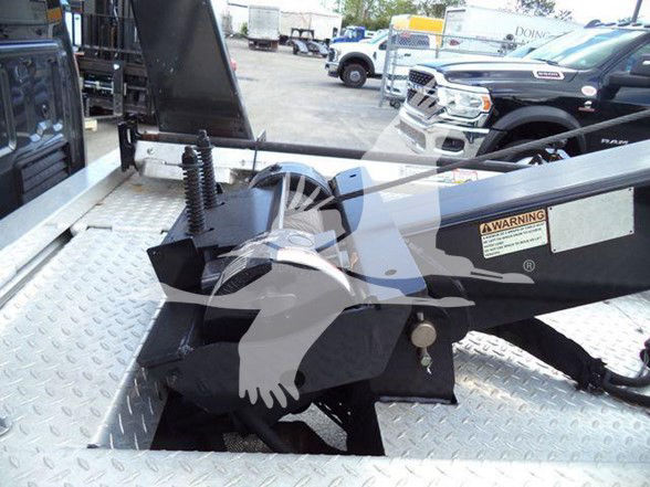 Ford F-450 tow truck flatbed with hydraulic winch and steel deck, showing a warning label and mechanism components.