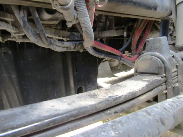Truck engine bay view showing electrical wires and frame member with hoses, frame rails, and components in the undercarriage.