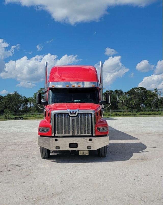 Front view of a red 2023 Western Star 4900 truck in a parking lot with a large chrome grille, black windshield, and silver bumper; visible license plate at front.
