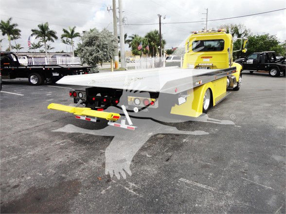 Tow truck flatbed with bright yellow cab, rear view shows flatbed and rear towing apparatus.
