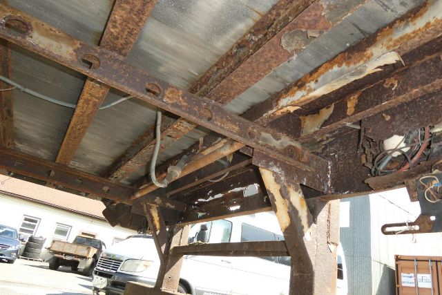 Trailer undercarriage showing rusted steel frame and cross members with wiring; side rail and wheel well visible.